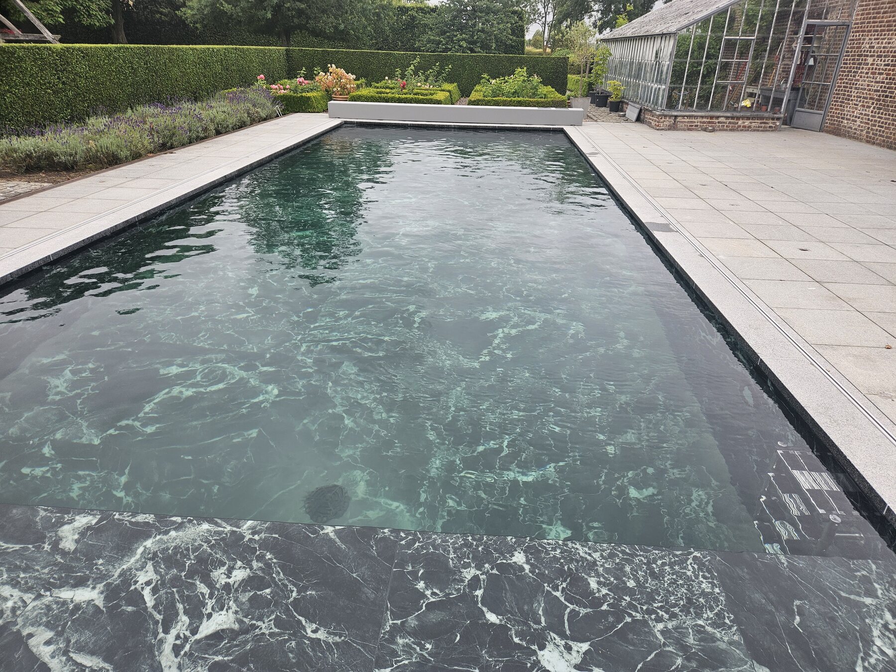 Gerenoveerd zwembad met donkere boord en lichte bestrating, eigen project van Sublime Pools